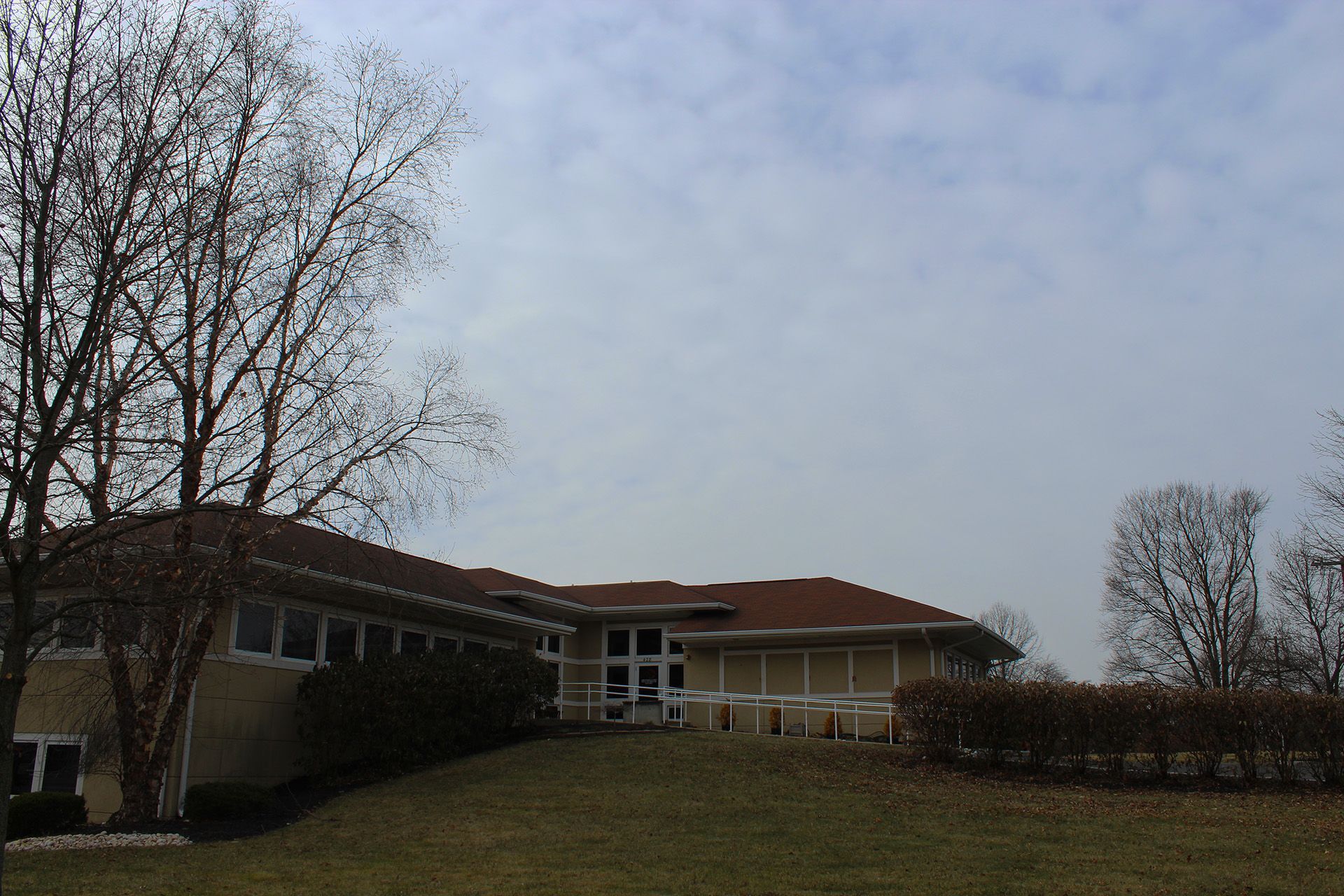 A large house with a red roof sits on top of a grassy hill
