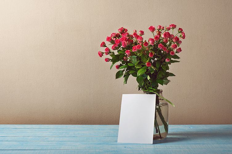 A vase filled with red roses and a card on a blue wooden table.