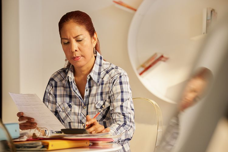 A woman is sitting at a table with papers and a calculator.