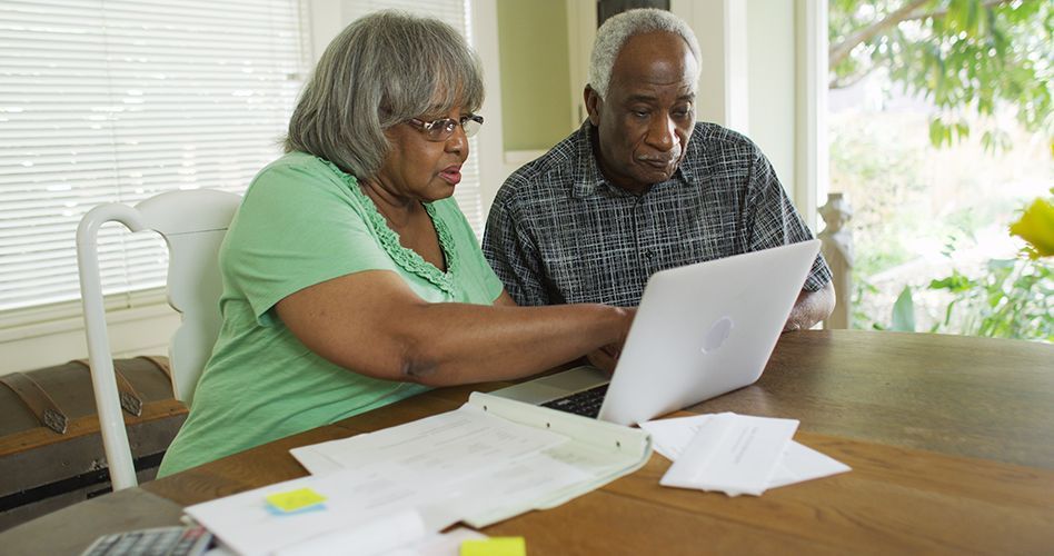 An elderly couple is sitting at a table looking at a laptop computer.