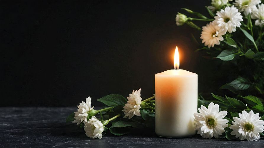 A lit candle is surrounded by white flowers on a table.