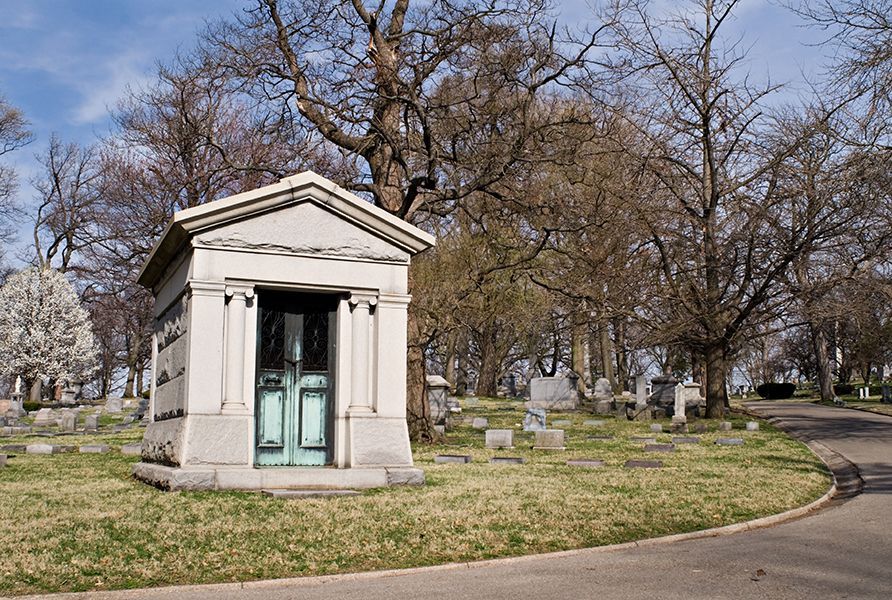 A small white building with a green door is in the middle of a cemetery.