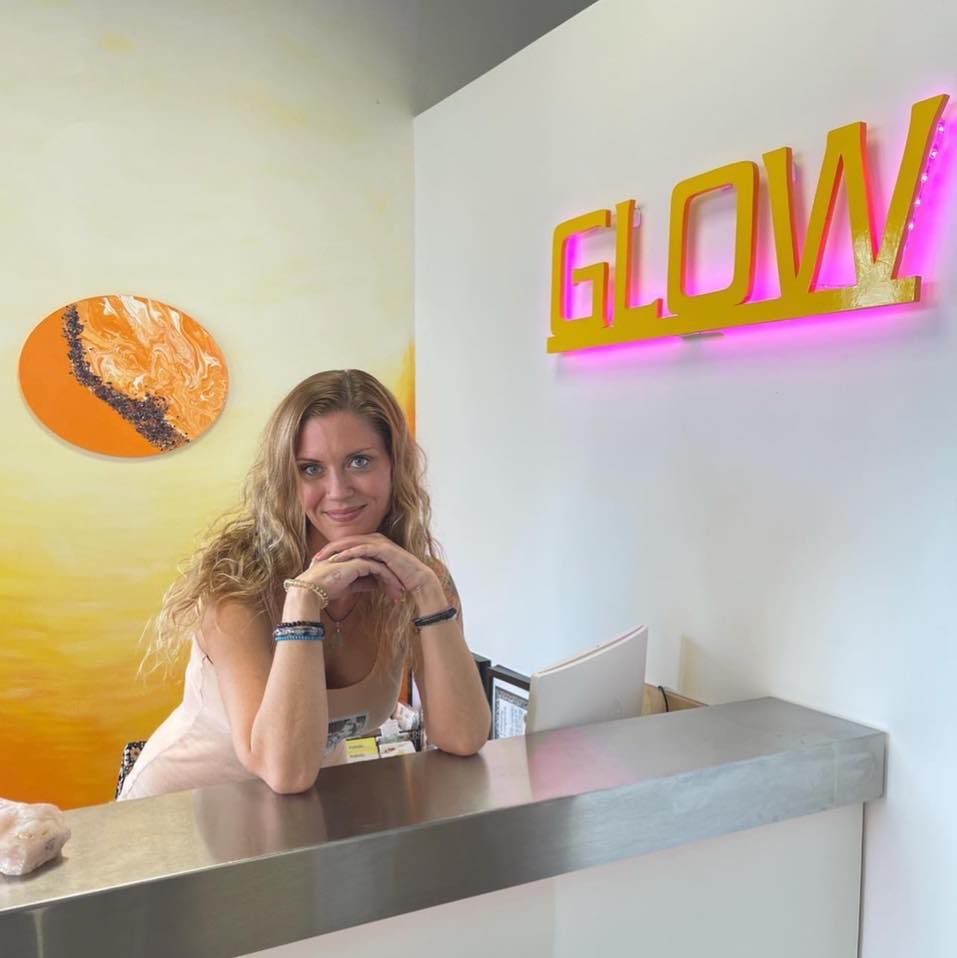A woman sits at a counter in front of a sign that says glow
