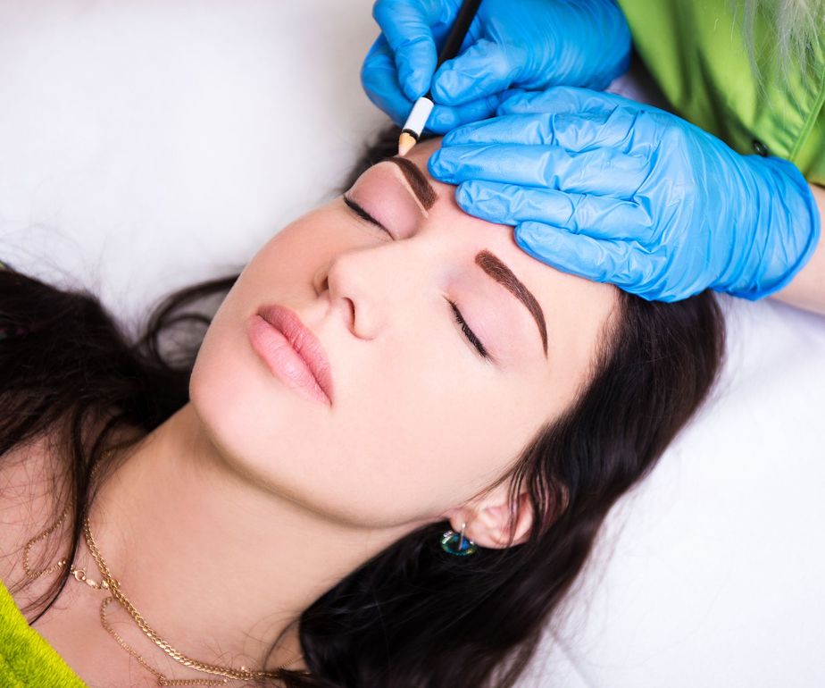 A woman is getting her eyebrows tattooed in a beauty salon.