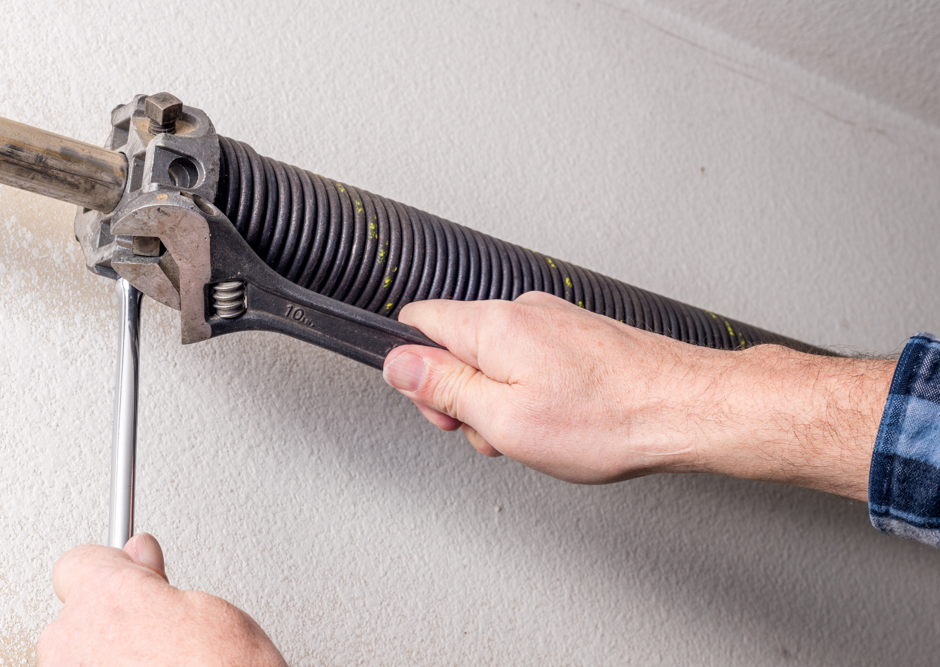 A man is fixing a garage door spring with a wrench.