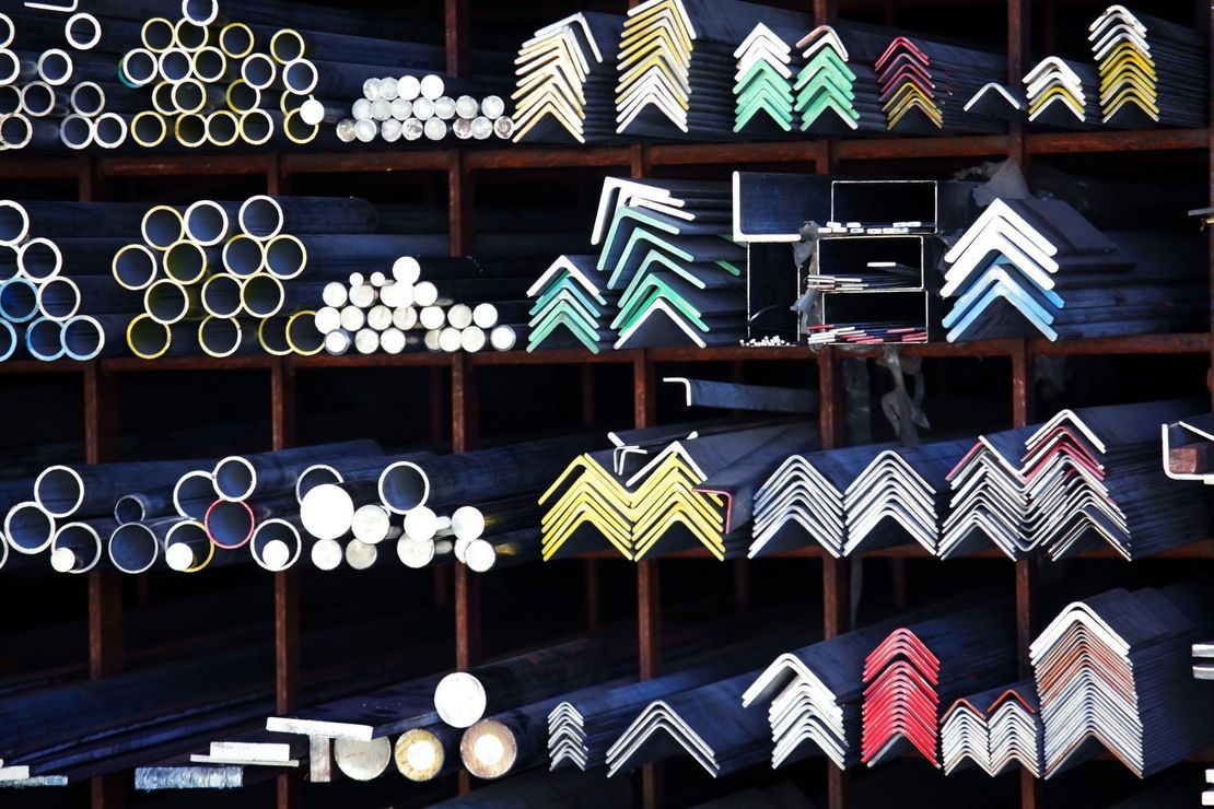 Scaffali pieni di varie forme metalliche, tra cui tubi, angolari e barre, in un negozio di forniture metalliche.