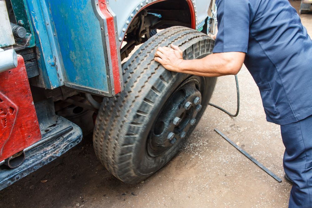 Mechanic Checking a Large Tire on a Blue Vehicle With a Red Body Panel — Mareeba Tyre Centre in Mareeba, QLD