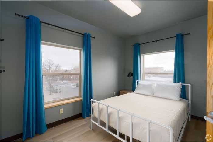 A bedroom with a bed , two windows and blue curtains.