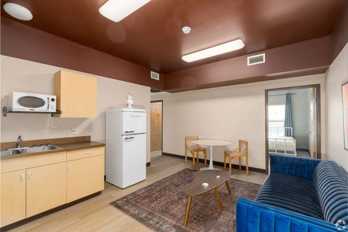 A living room with a couch , table , refrigerator and microwave.