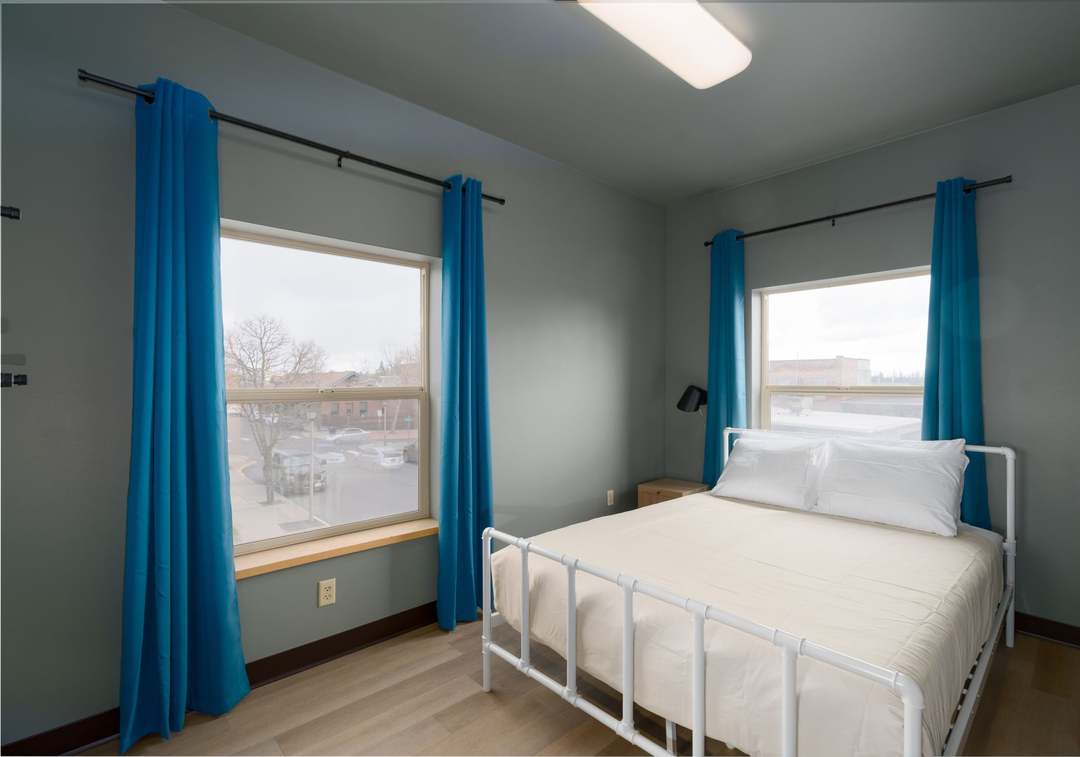 Bedroom with blue curtains, white bed frame, and two windows.