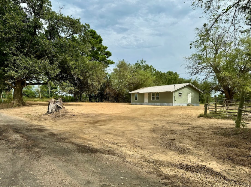 A house is sitting in the middle of a dirt field surrounded by trees.
