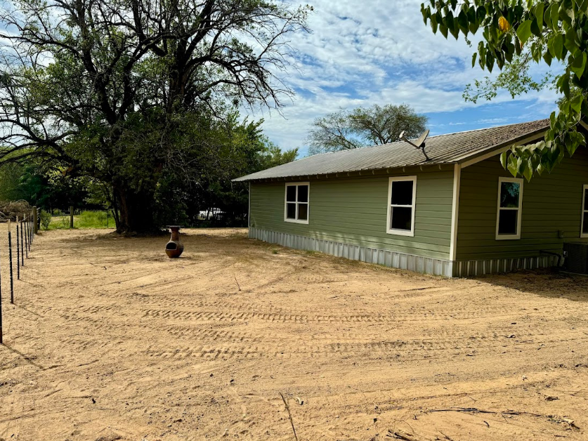 A green house is sitting in the middle of a dirt field.