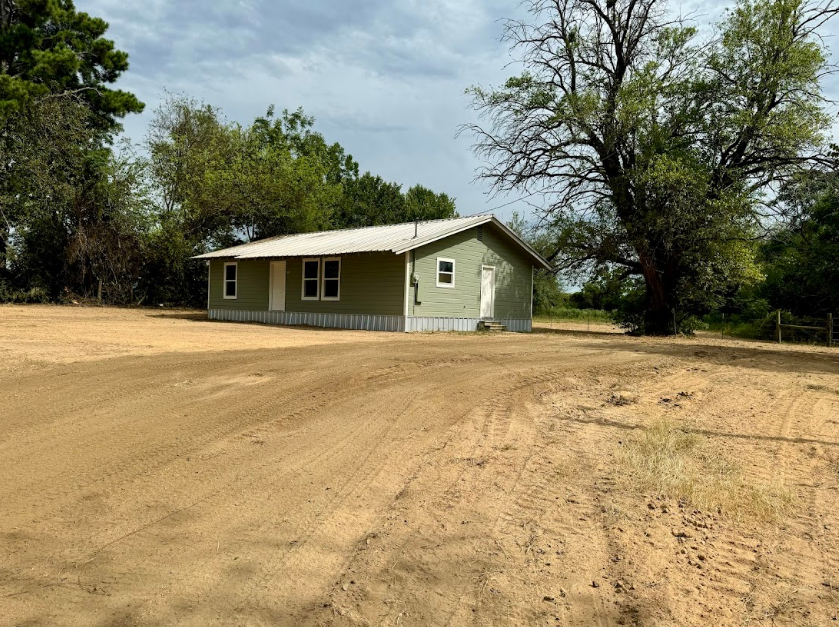 A green house sits in the middle of a dirt field