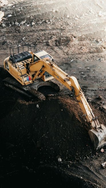 Yellow excavator digging into dark earth.