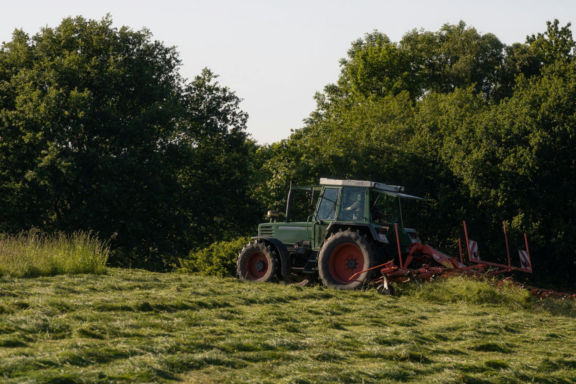 A green tractor is plowing a field of grass.