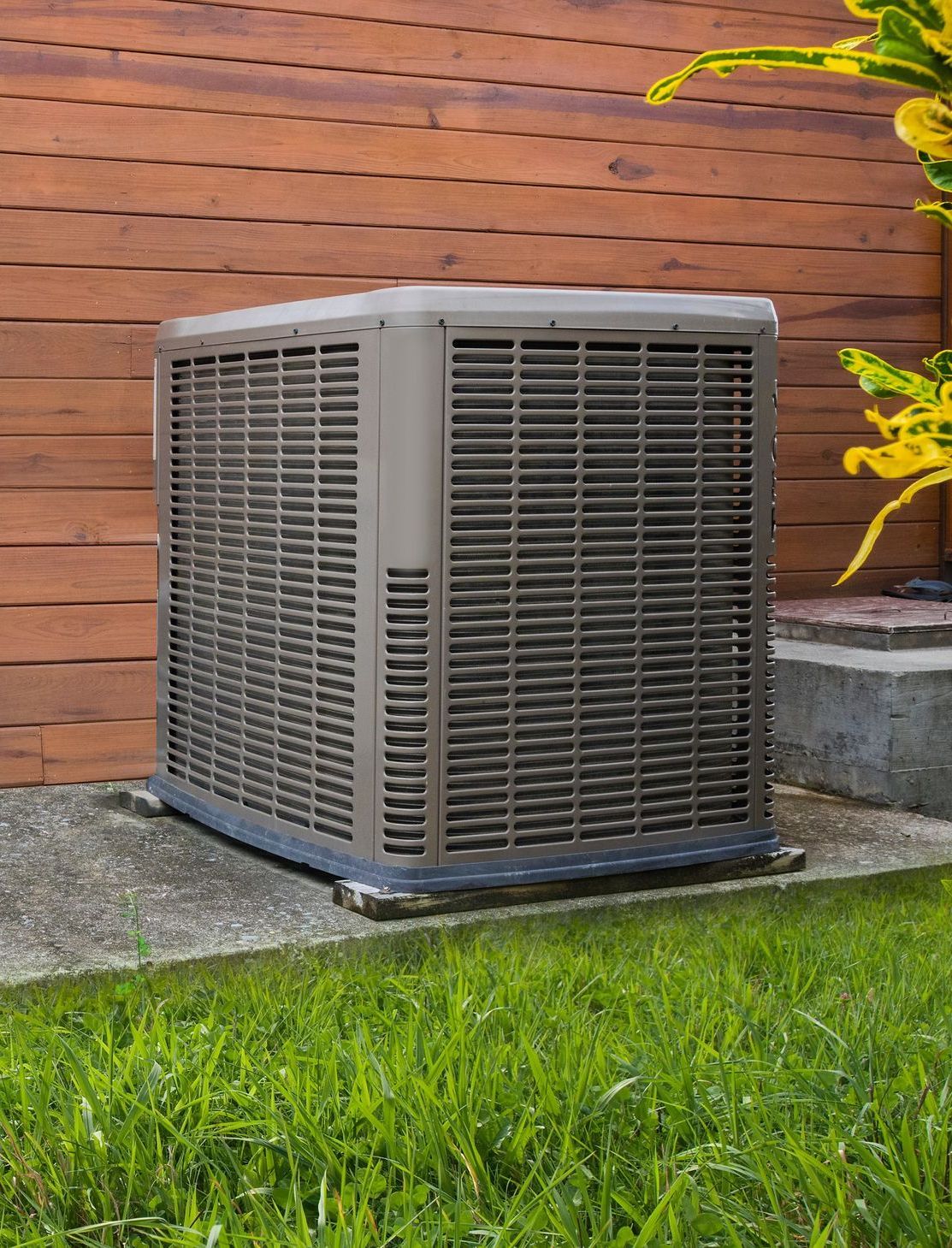 Un grand climatiseur est posé dans l'herbe devant un bâtiment en bois.