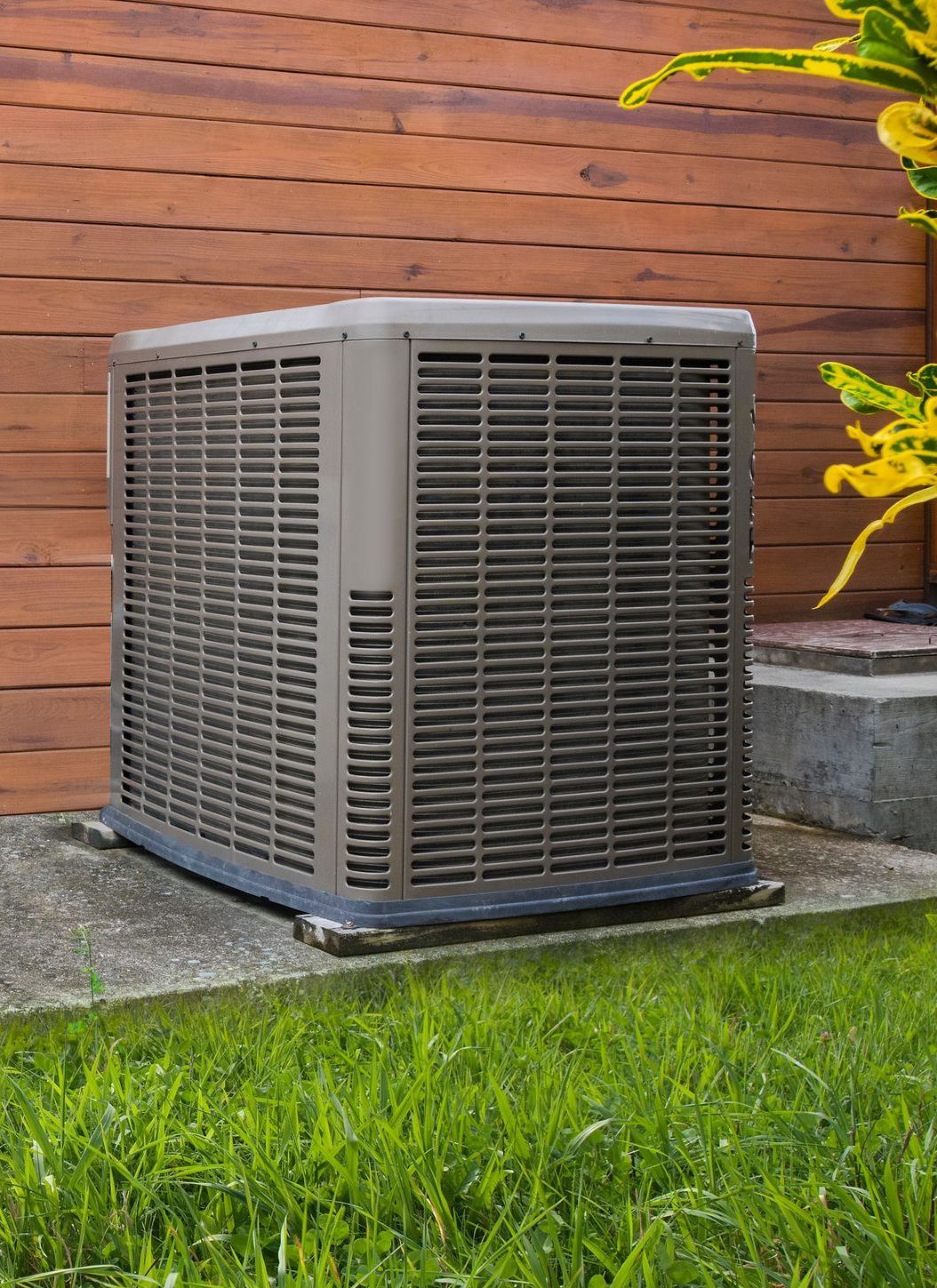 Un grand climatiseur est posé dans l'herbe devant un bâtiment en bois.