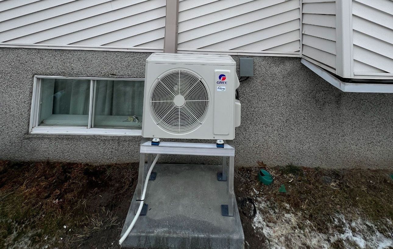 Un climatiseur blanc est monté sur le côté d'un bâtiment à côté d'une fenêtre.