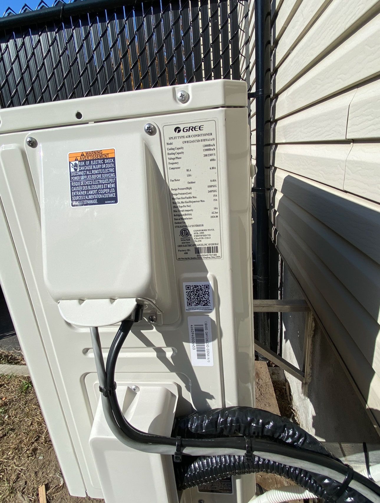Un climatiseur blanc est installé à l'extérieur d'une maison à côté d'une clôture.