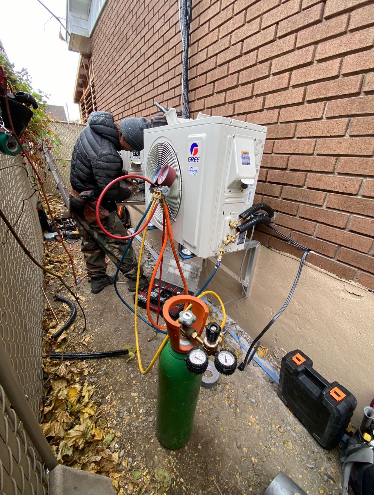 Un homme travaille sur un climatiseur à l'extérieur d'un bâtiment en briques.
