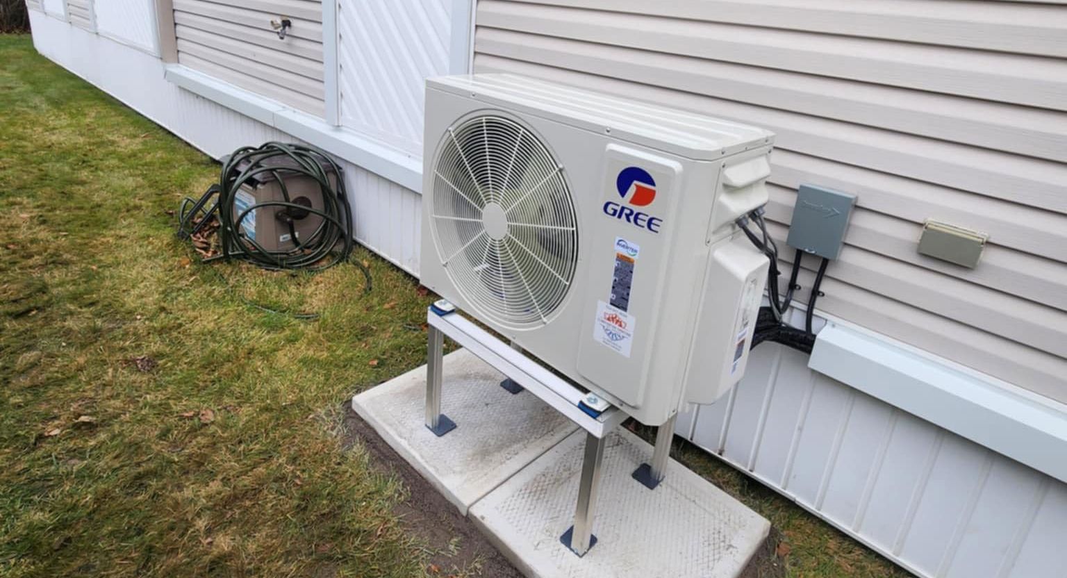 Unité de climatisation Gree sur une base en béton à l'extérieur du bâtiment avec de l'herbe verte.