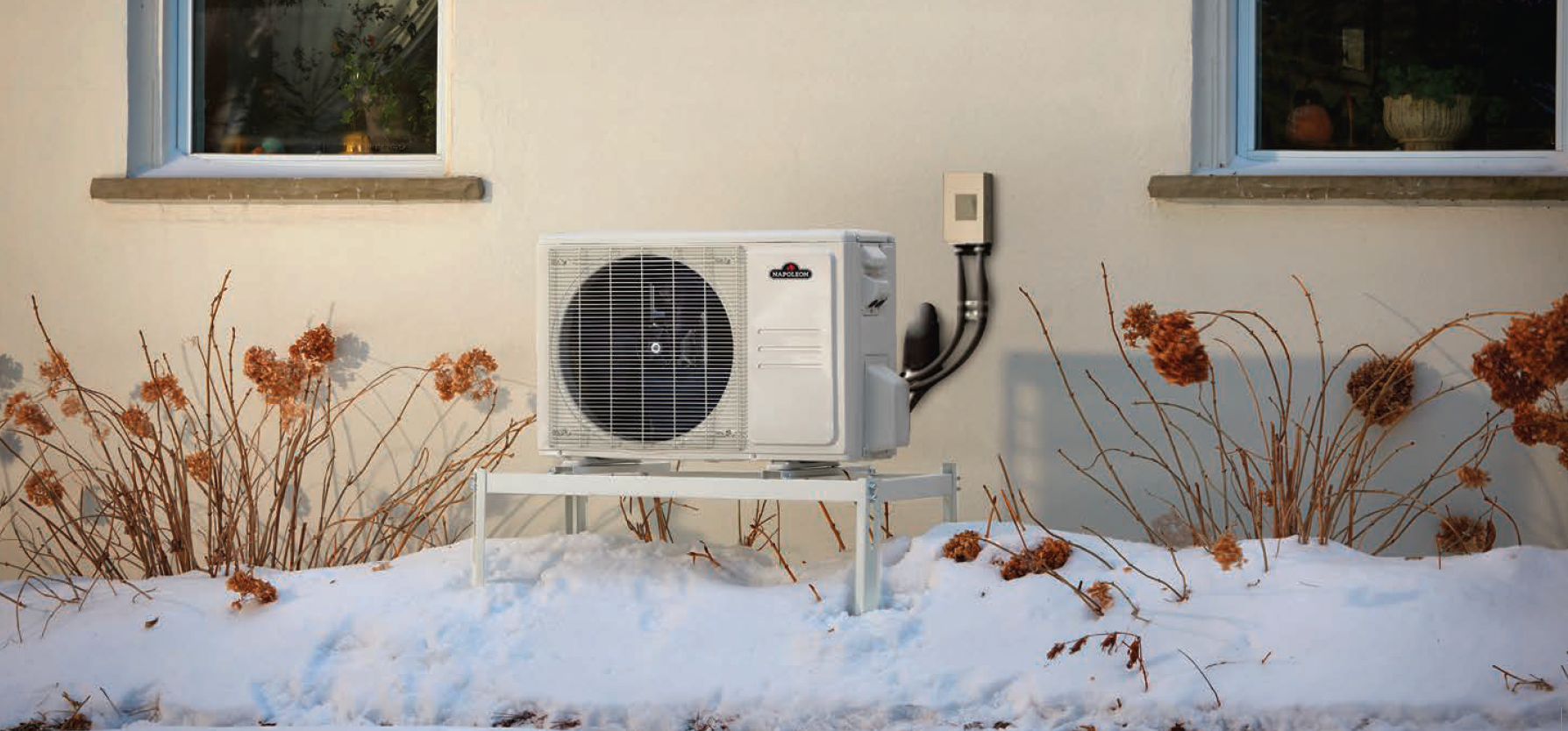 Un climatiseur à l'extérieur d'un bâtiment dans un décor hivernal avec de la neige et des branches nues.