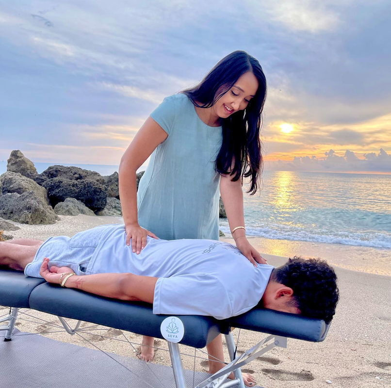 Woman giving a back massage on a beach at sunset