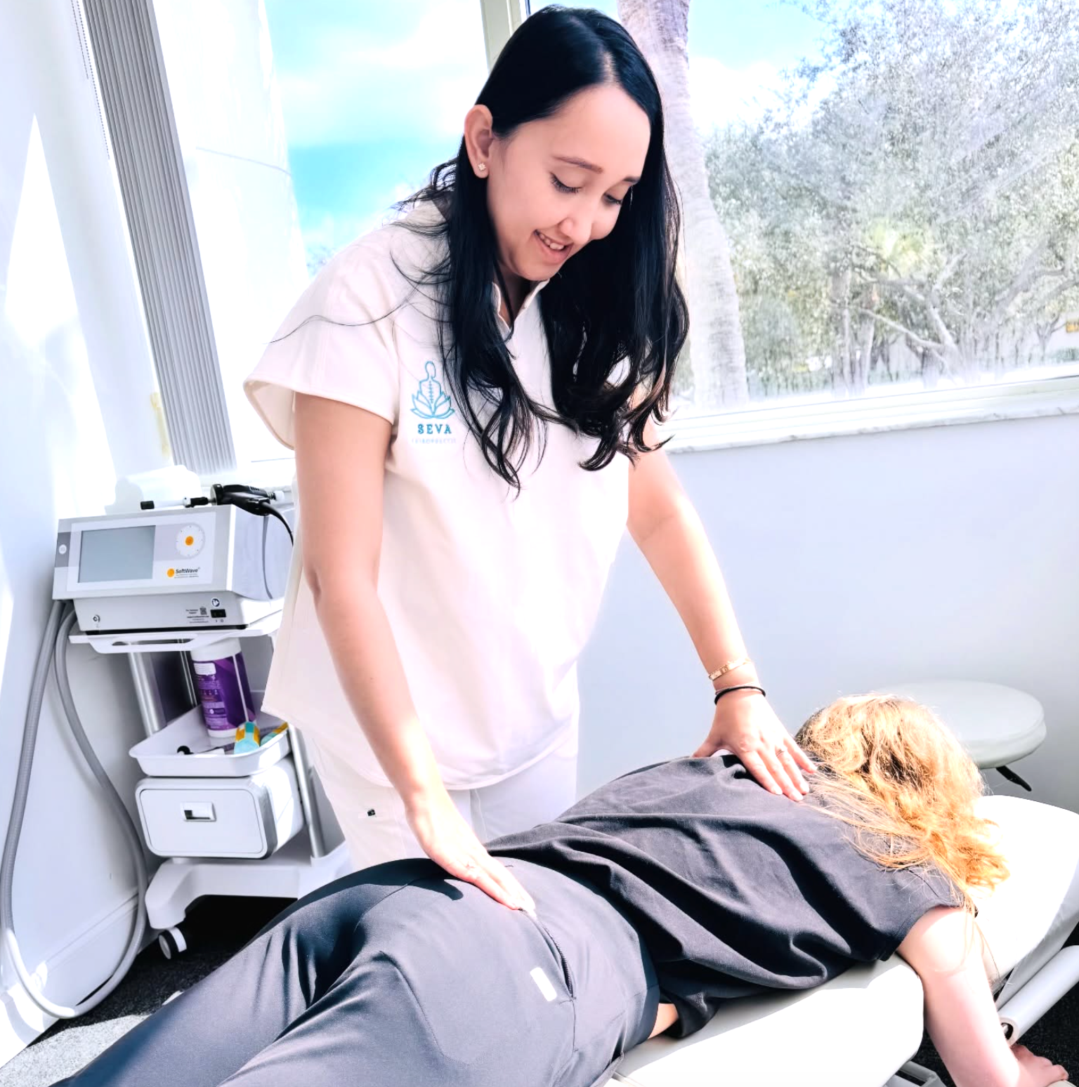 Therapist adjusting a patient on a treatment table in a bright clinic with a window view