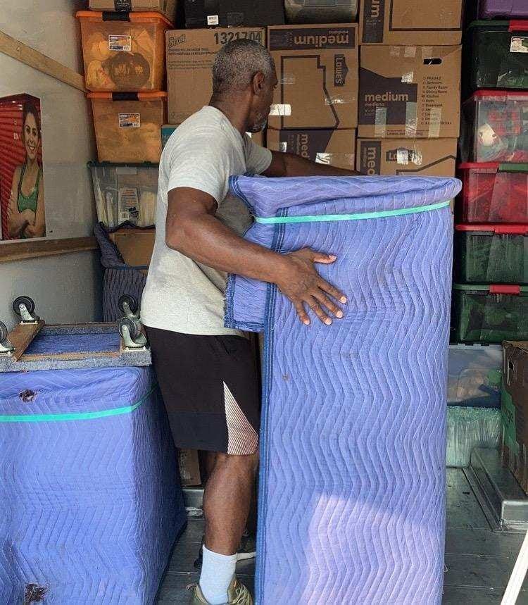 A man is carrying a large purple box in a warehouse.