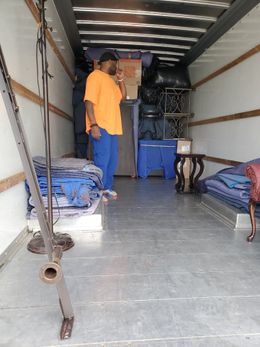 A man is standing in the back of a moving truck talking on a cell phone.