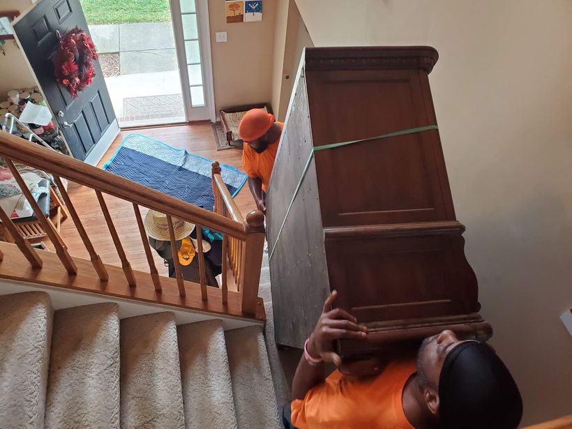 A man is carrying a large wooden cabinet up a set of stairs.