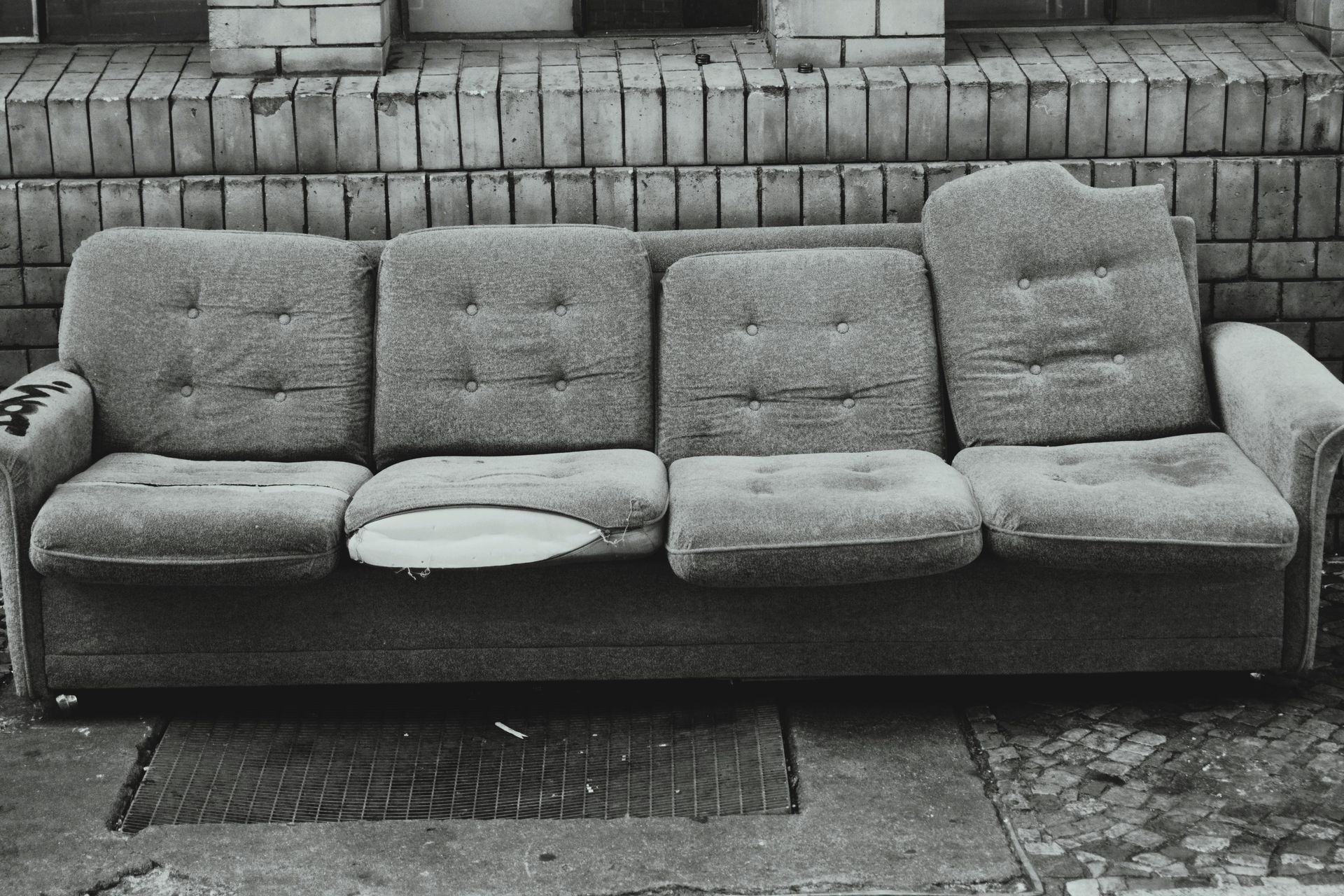 A black and white photo of a couch with a broken arm rest