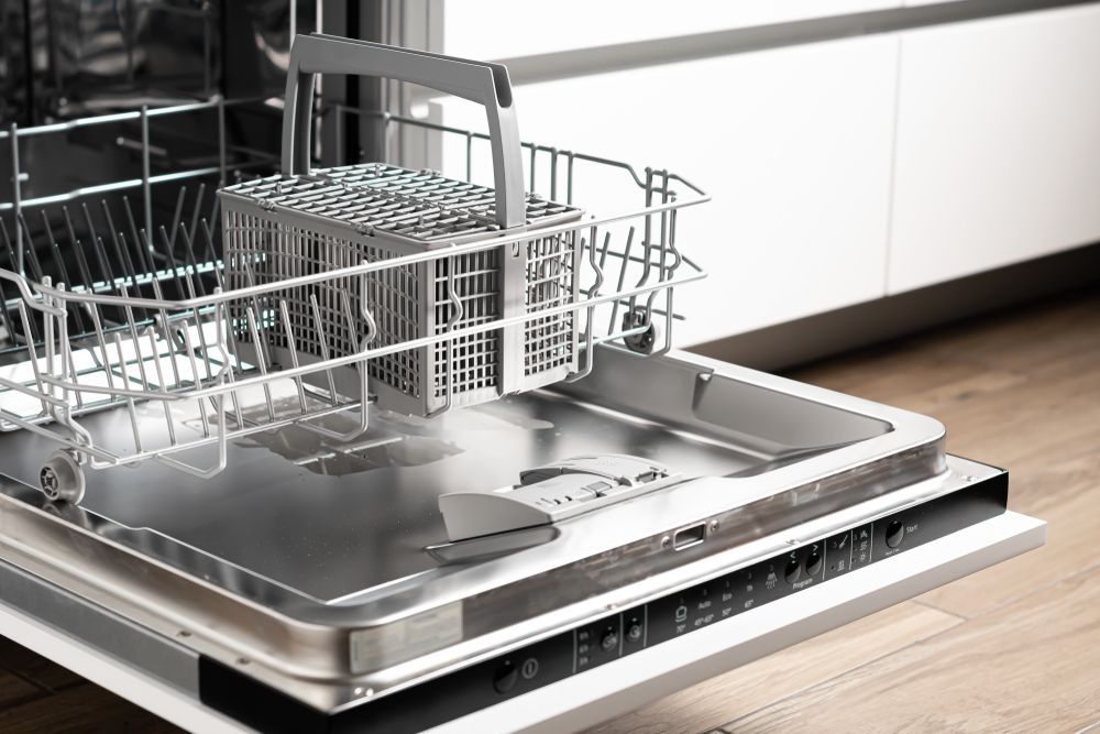 A dishwasher with the door open is sitting on a wooden floor in a kitchen.
