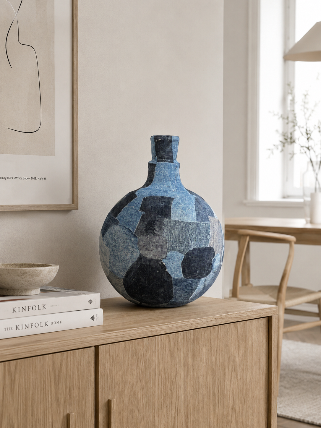 Blauwe mozaïekvaas op een houten kast in een lichte, minimalistische kamer.