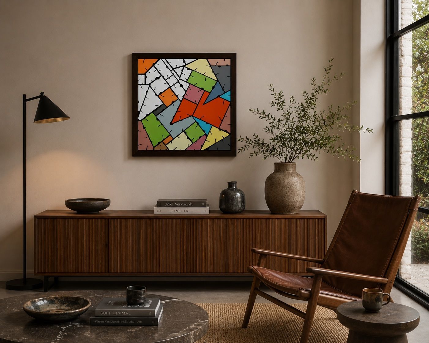 Een ingelijst, vierkant abstract kunstwerk met geometrische, veelkleurige segmenten hangt aan een witte muur boven een bureau.