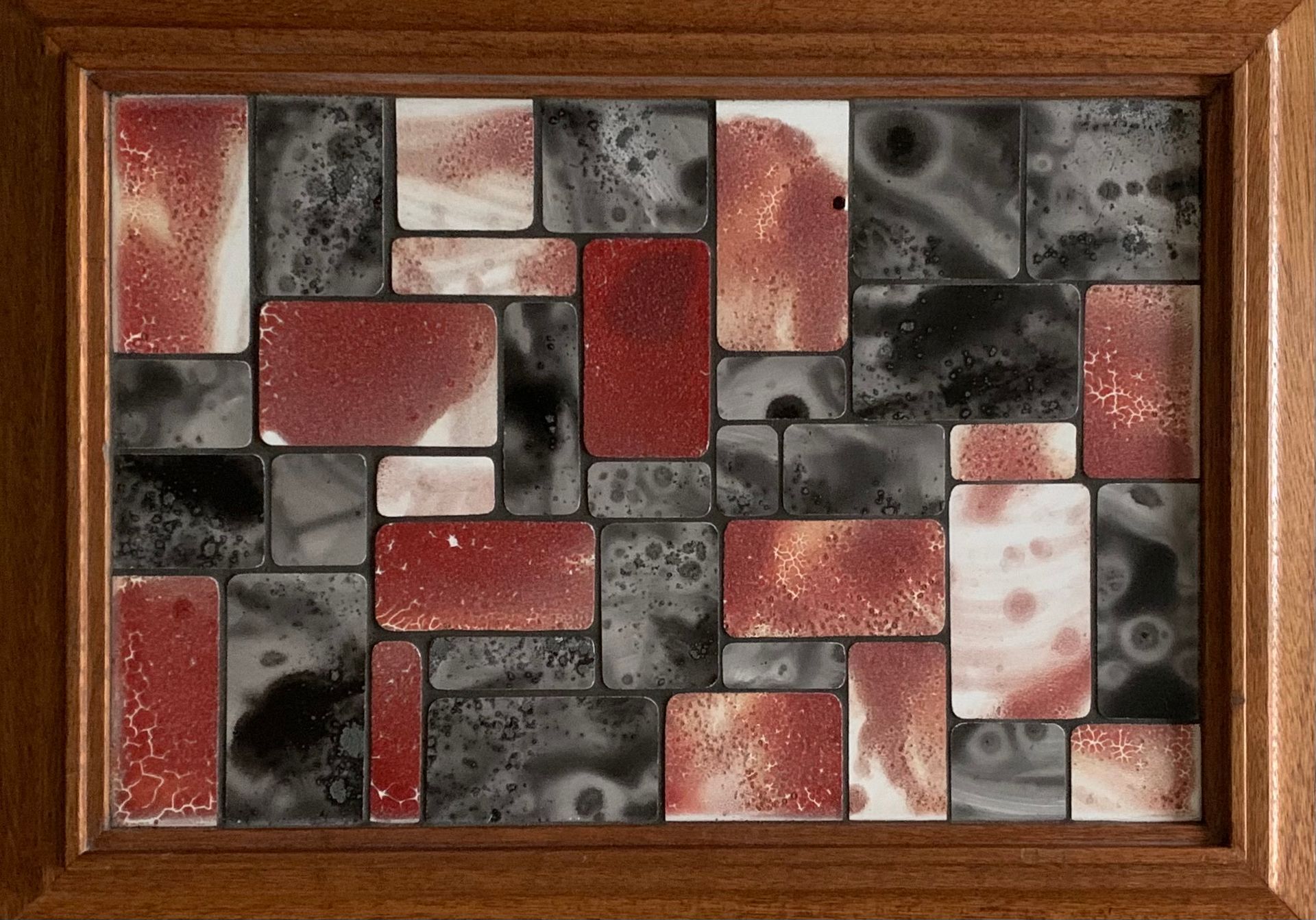 Een houten frame bevat een mozaïek van rode, zwarte en witte tegels