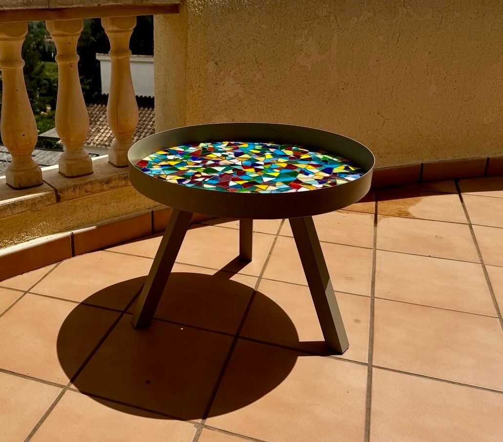 Een klein tafeltje met een kleurrijk blad staat op een betegelde vloer