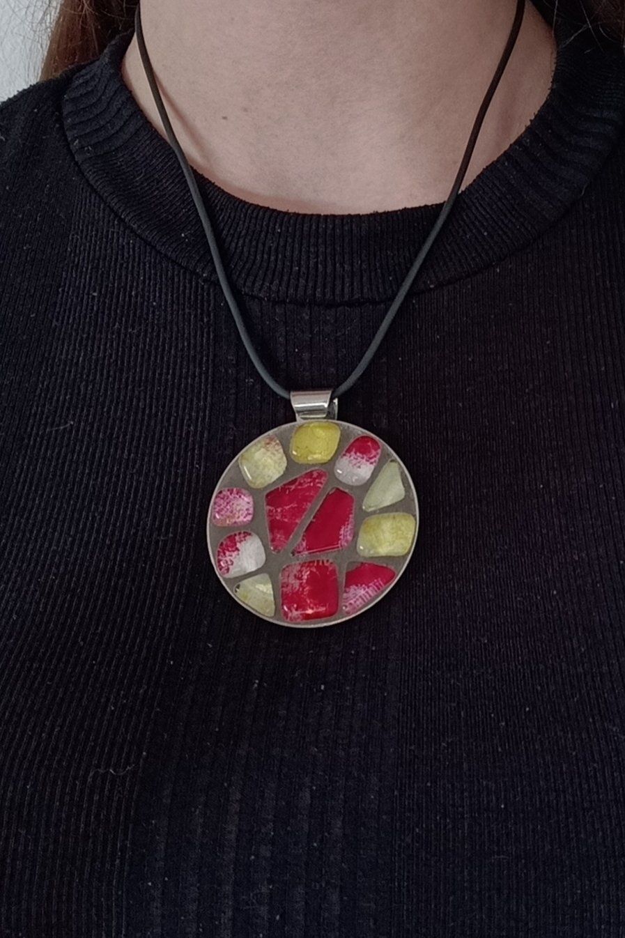 Een vrouw in een zwart shirt en een ketting met een mozaïekhanger