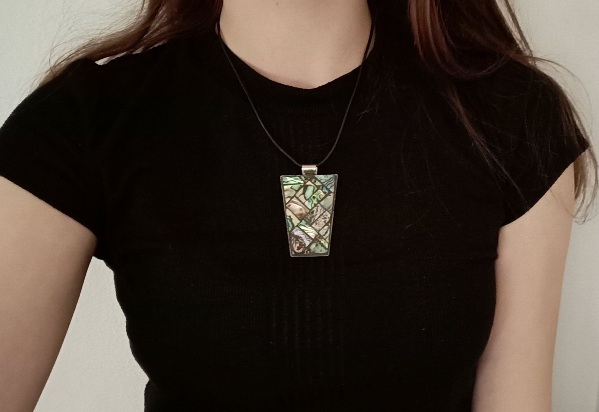 Een vrouw in een zwart shirt en een ketting met een mozaïekhanger