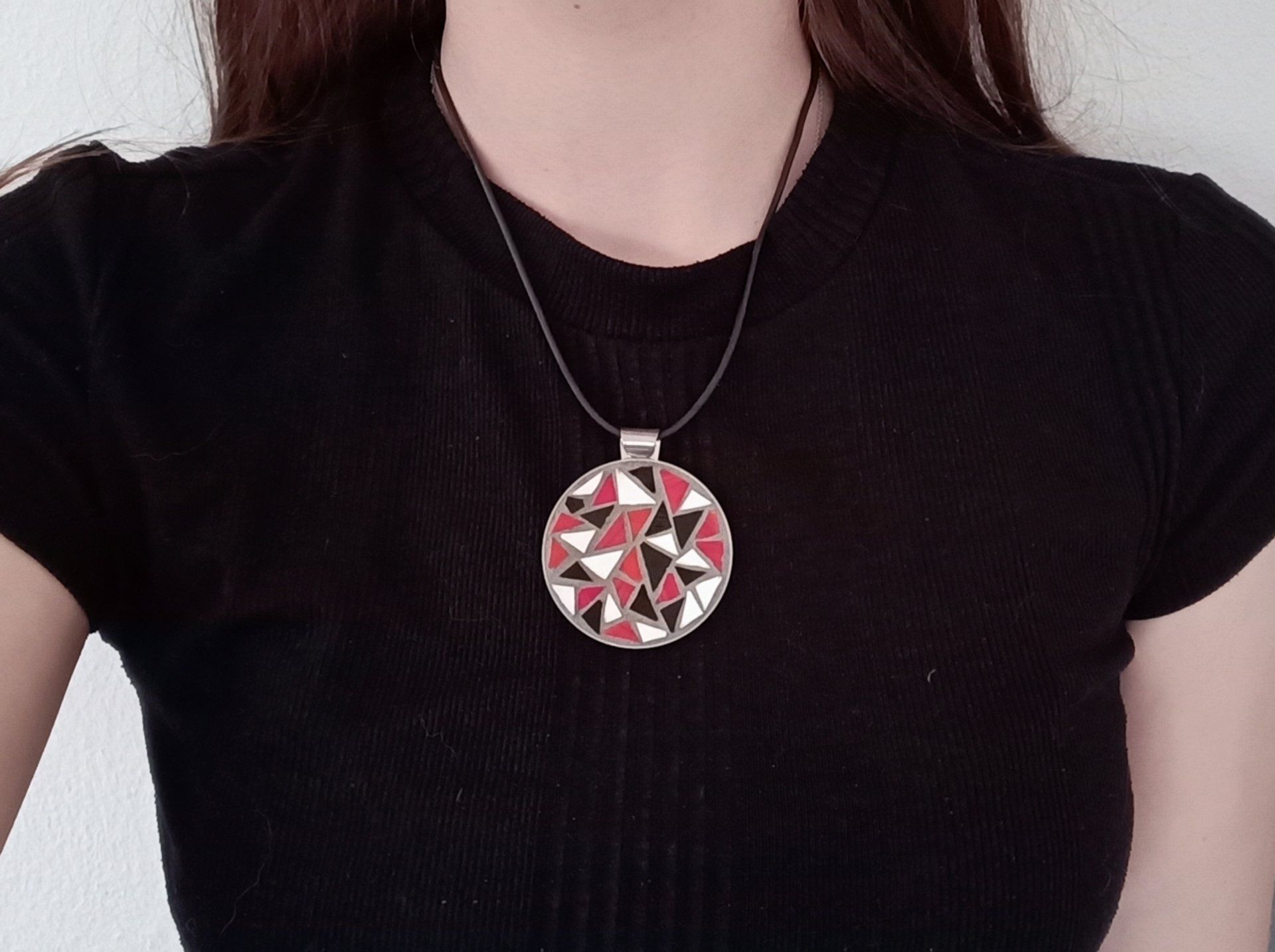 Een vrouw in een zwart shirt en een ketting met een mozaïekhanger