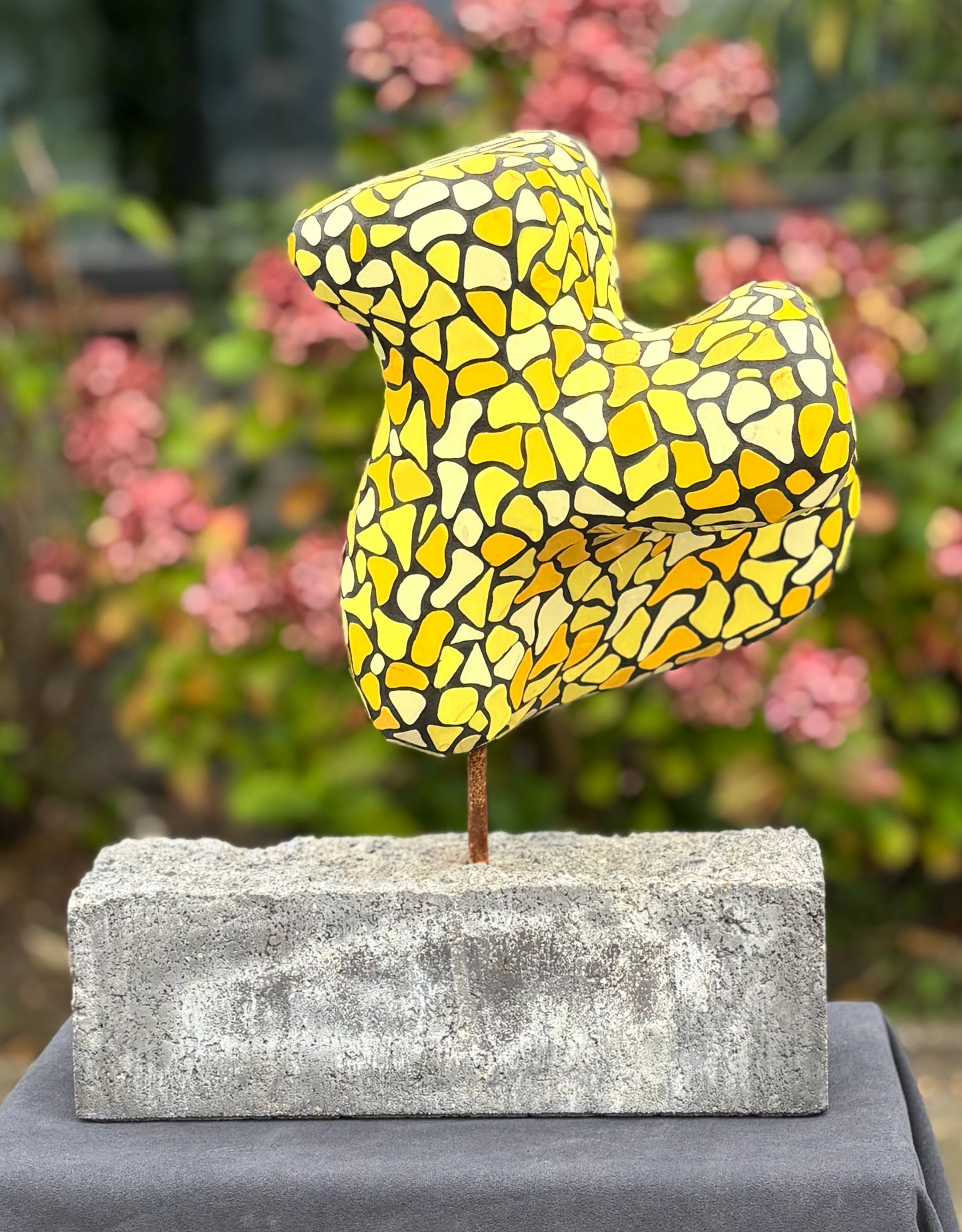 Een geel mozaïekbeeldhouwwerk staat op een betonnen blok
