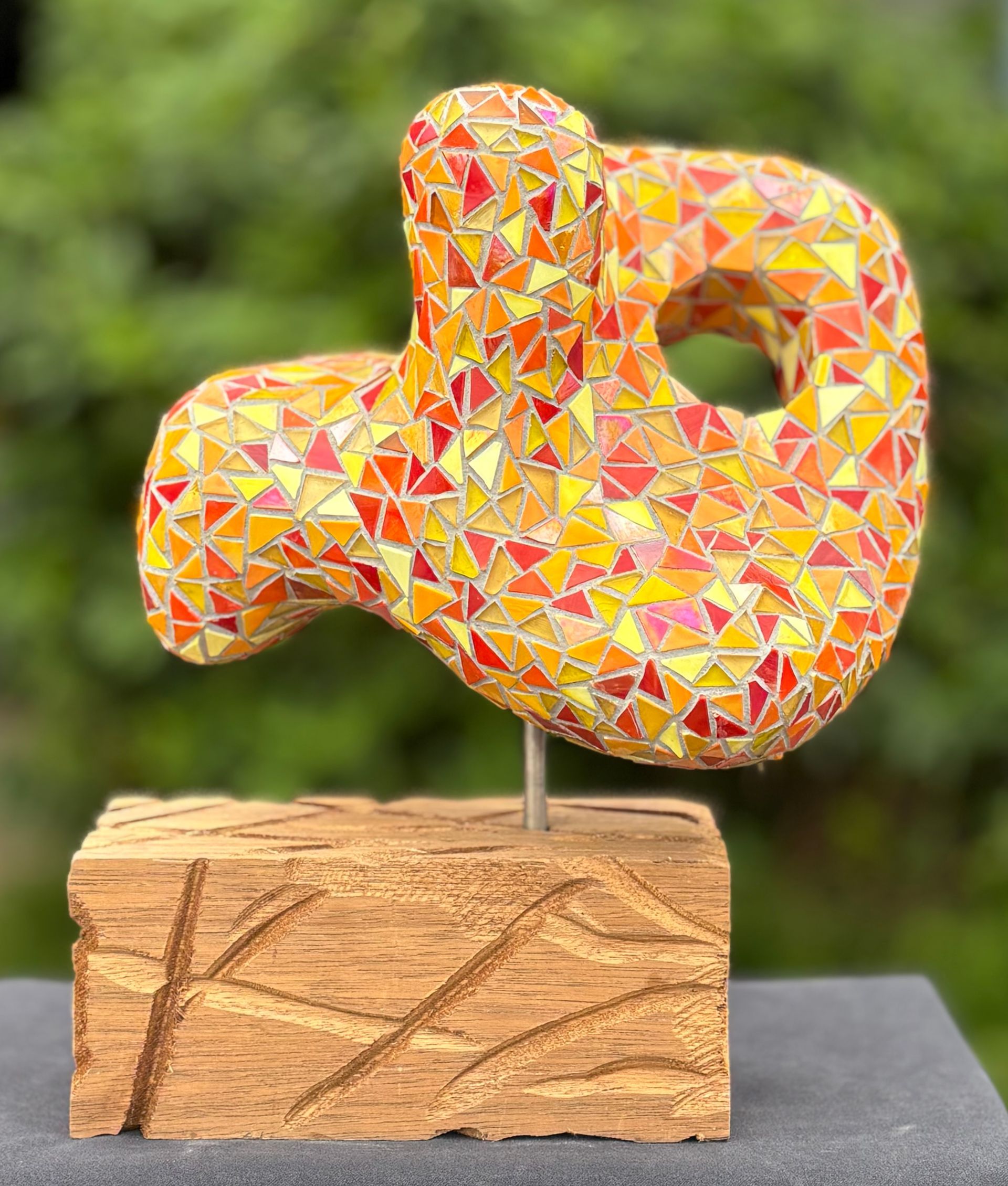 Een mozaïeksculptuur staat op een betonnen sokkel.