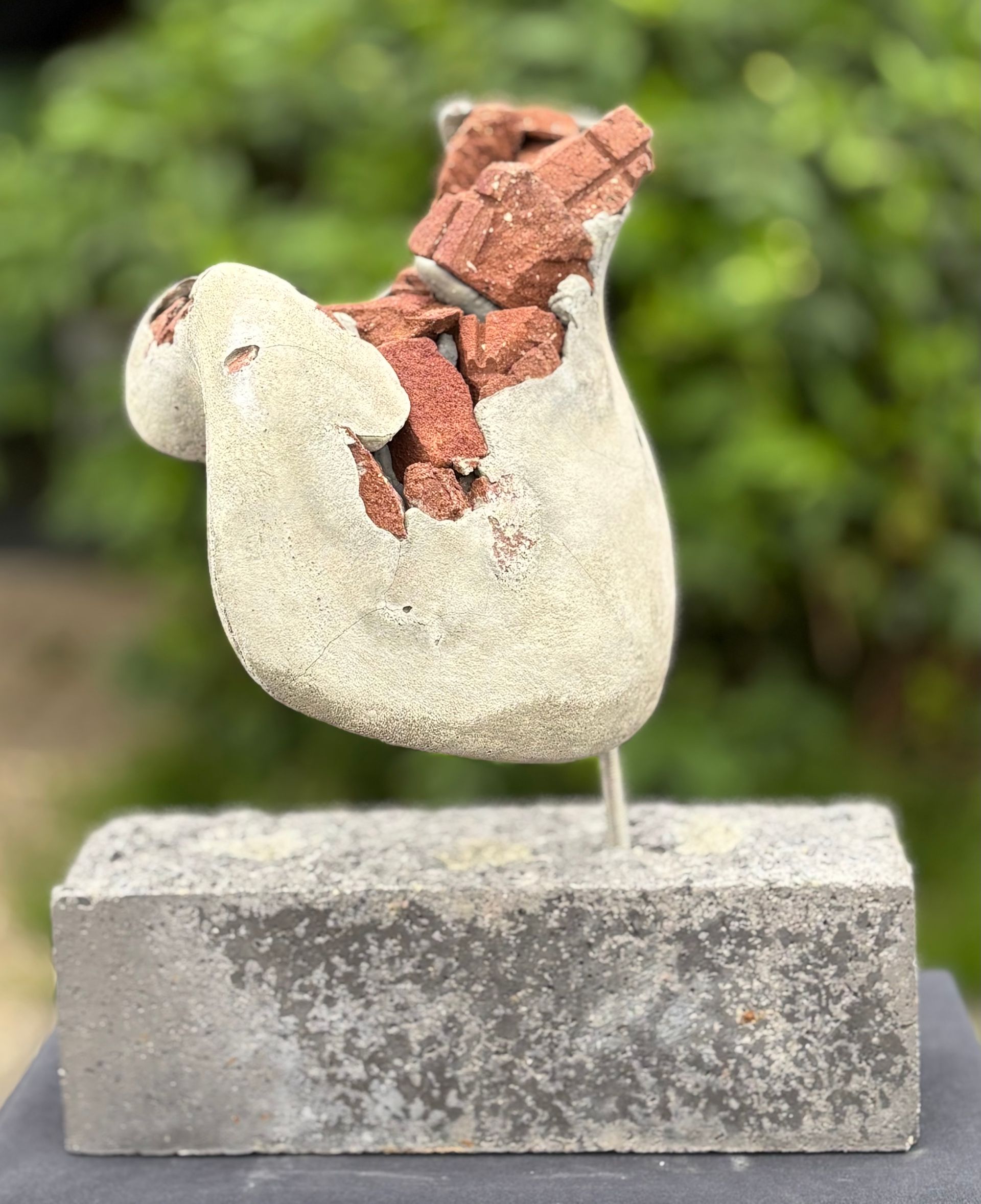 Een standbeeld van een kip zit bovenop een betonnen blok.