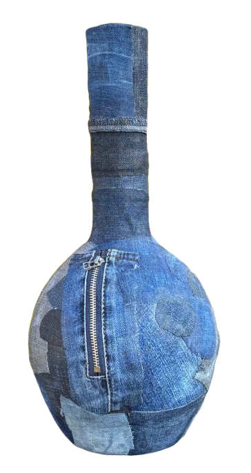 Een blauwe, gestructureerde, bolvormige vaas met een ritssluiting staat buiten tegen een achtergrond van gele bloeiende struiken.