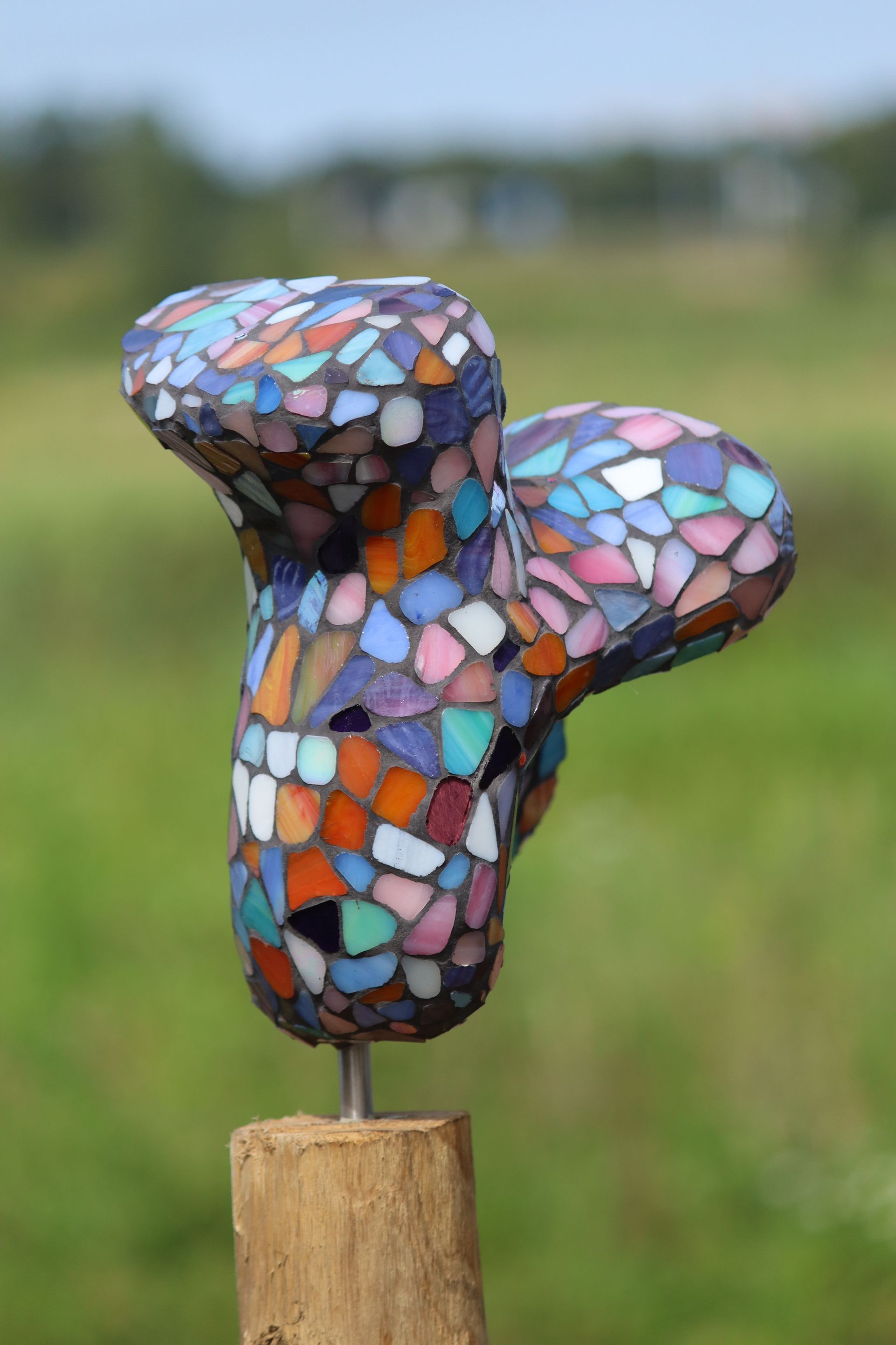 Een kleurrijk beeld staat op een houten paal in een veld.