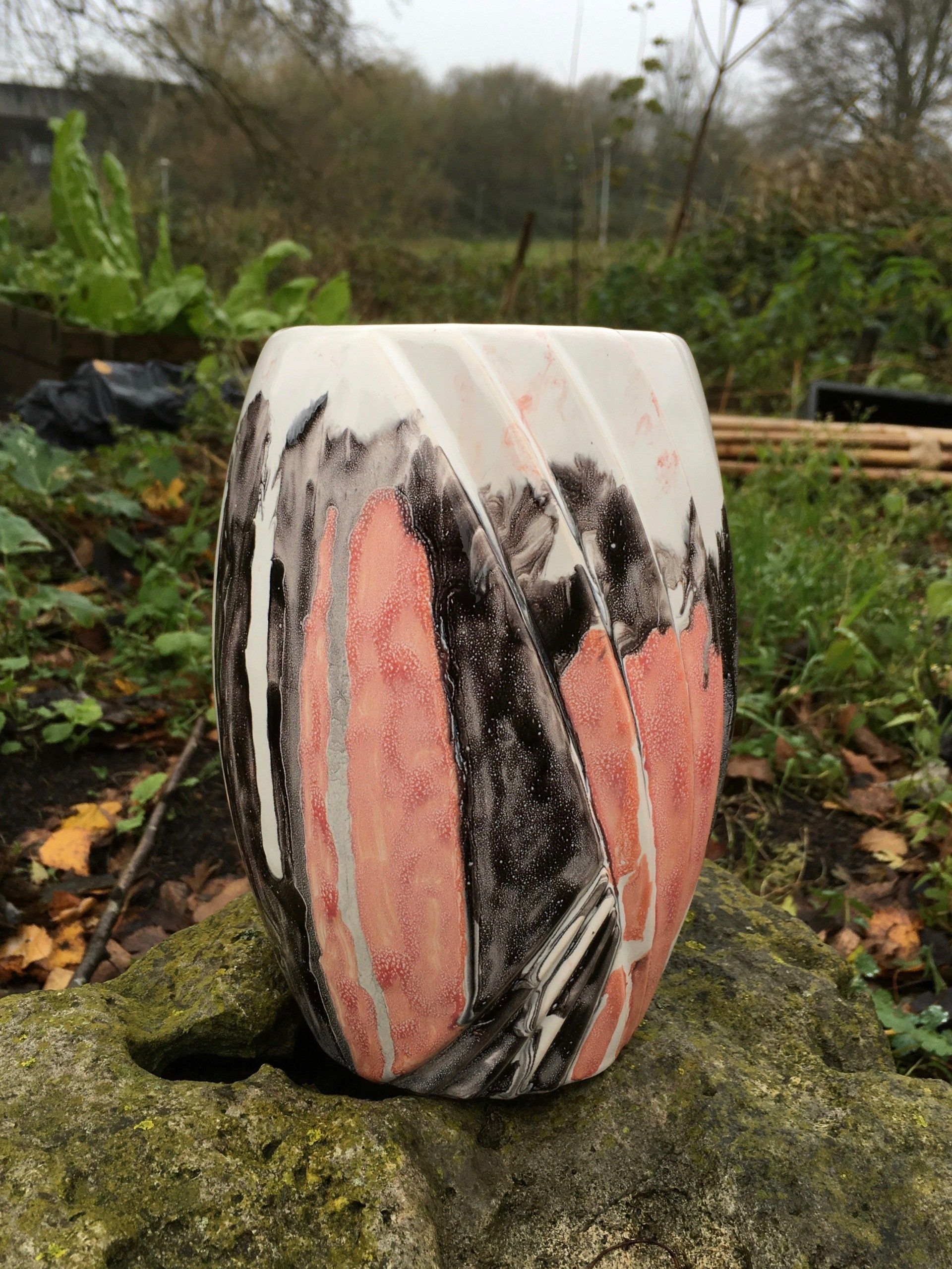 Een roze en zwarte vaas staat op een rots.