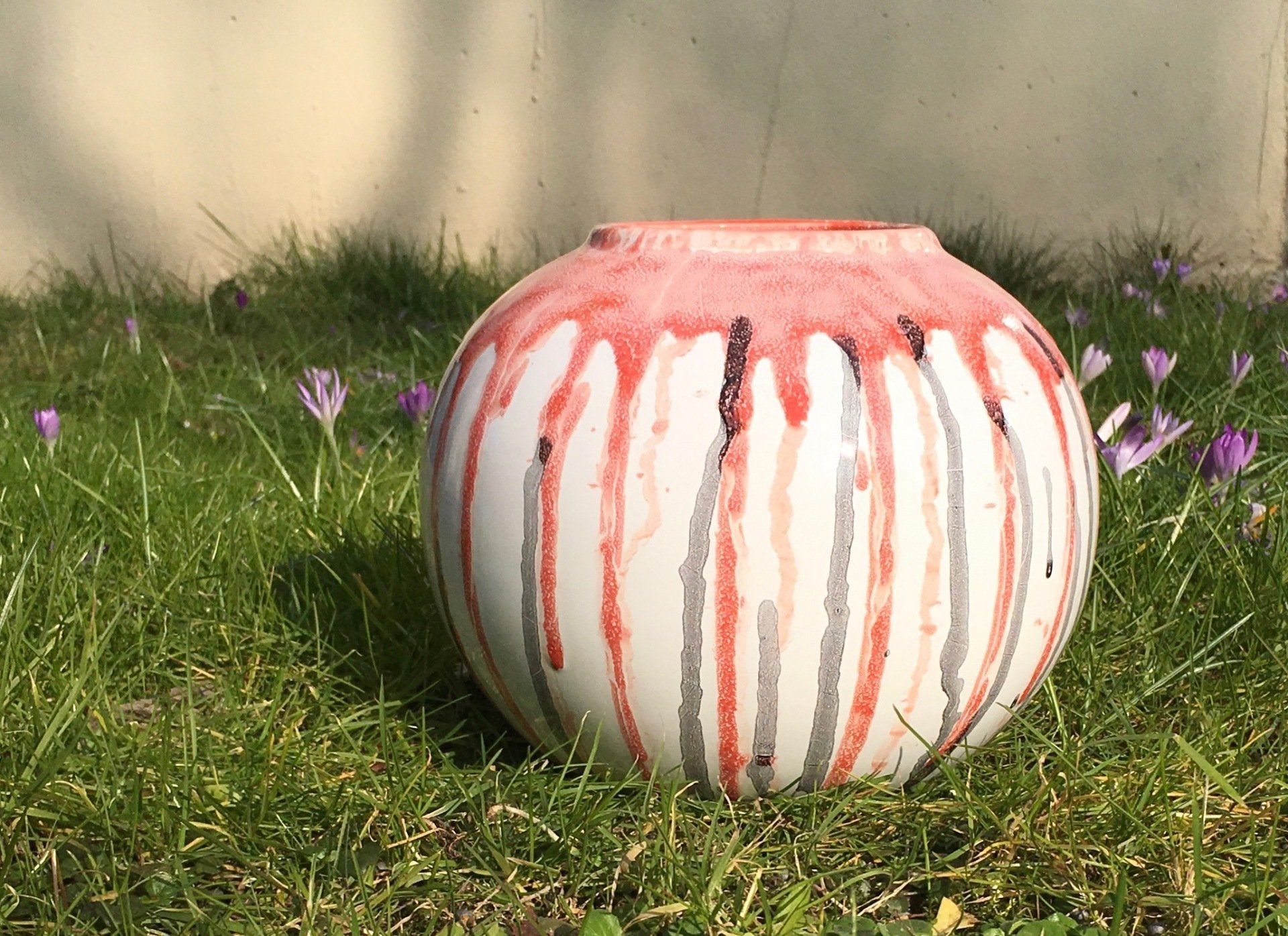 Een rood-wit gestreepte vaas staat in het gras.