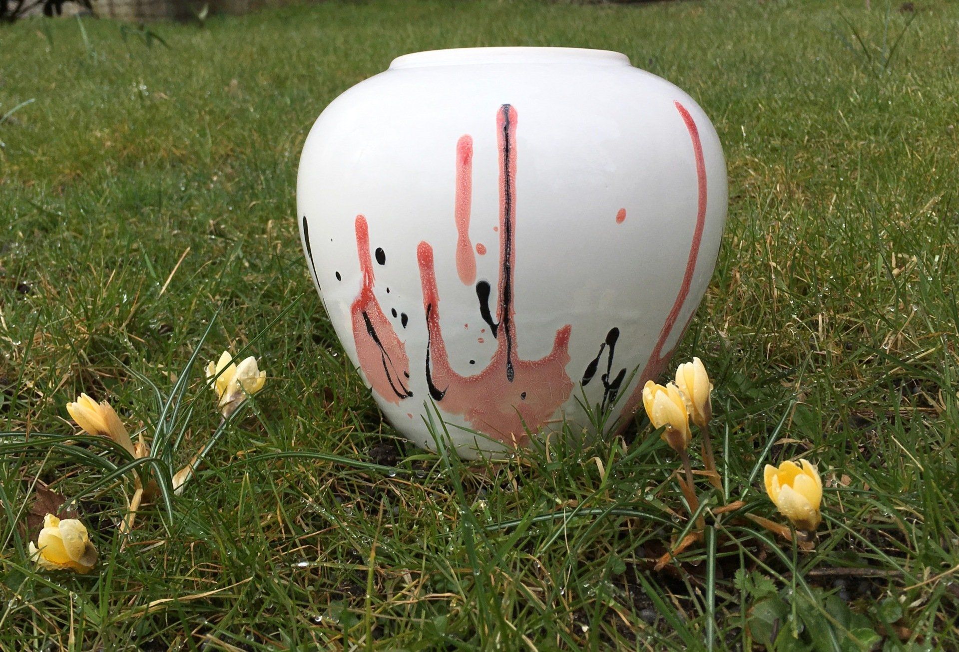 Een witte vaas met rode vlekken erop staat in het gras