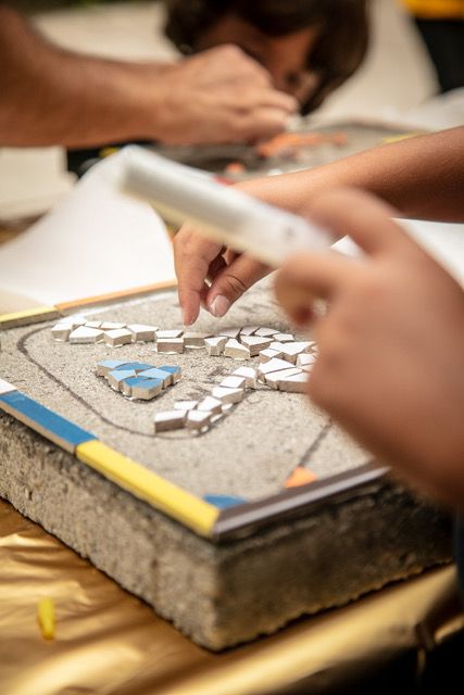 Een groep mensen werkt op een tafel aan een mozaïek.