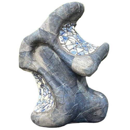 Een abstracte sculptuur in donkerblauw met textuur en geometrische blauw-witte tegelaccenten, geplaatst tegen een wazige groene achtergrond.